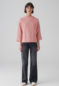 Maglia a herringbone rossa e bianca con maniche corte e collo alto, abbinata a jeans a gamba larga scuri e sneakers bianche.
