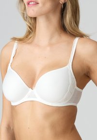 Valgbra valkoisella pehmustuksella, jossa on pitsireunus olkaimissa. Sileä kangas, luitepohjainen tuki ja hakasuljenta takana.