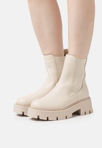 Bottines beiges à chevilles avec des panneaux latéraux élastiques, une finition en cuir lisse et des semelles épaisses avec une texture striée pour une meilleure adhérence.