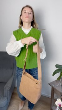 Bolsa de ombro em camurça castanha com uma alça longa, um bolso com fecho na frente e uma textura suave. Colete de malha em verde, sobre uma blusa branca.