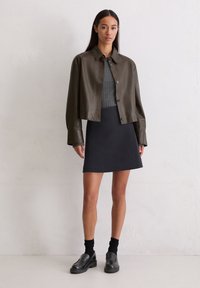 Ciemnozielona skórzana kurtka typu cropped, szary sweter, czarna dopasowana spódnica i czarne loafersy na grubej podeszwie, zestawione z czarnymi skarpetkami.