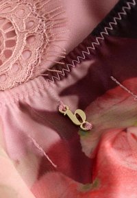 Material satinat roz cu model floral, decorat cu detalii din dantelă și un accesoriu de culoare aurie prins cu ață roz, prezentând cusături fine.