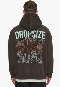 Brun hoodie med gentagne "DROPSIZE"-tekster i forskellige farver på ryggen, med et afslappet fit og en hætte med snore.