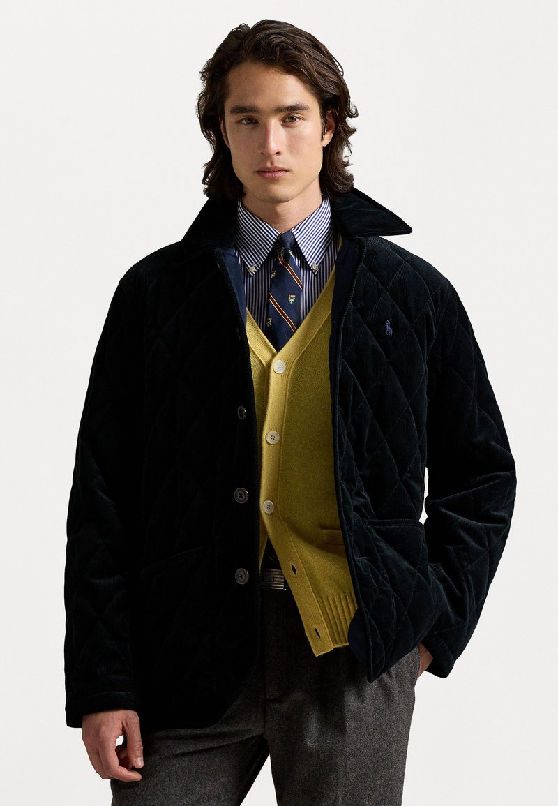 Melna kvadrāta samta jaka ar apkakli, valkāta virs zaļa kardigāna un zila striķota krekla. Iespējas ar pogu aizdari un kabatām.