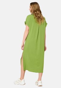 Abito maxi verde a maniche corte con spacchi laterali, caratterizzato da una vestibilità comoda e da una textura liscia. Abbinato a scarpe da ginnastica bianche.