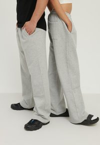 Hallid dressipüksid, mis on valmistatud pehmest kangast, küljetaskudega, lõdva lõikega ja kergelt tekstureeritud pinnaga, sobitatud mustade jalanõudega.