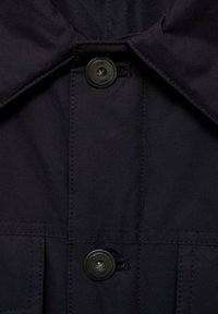 Dunkelblaue Jacke mit großem Kragen, zwei Knöpfen und dezenten Steppdetails. Das Material wirkt glatt und ist wahrscheinlich wasserdicht.