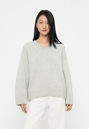 Grå strikkegenser med v-hals, oversized passform, ribbestrikkede mansjetter og kant. Stoffet har en subtil tekstur og små flekker gjennom hele.
