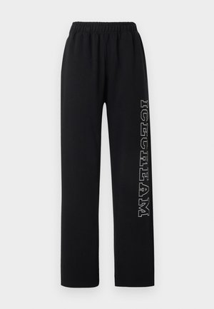 Zwarte joggingbroek met elastische tailleband en witte, gestippelde tekst "DREAM" die verticaal over het rechterbeen loopt tegen een effen achtergrond.