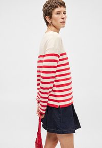 Sark ar sarkaniem un bēšiem svītrojumiem, ar garām piedurknēm un brīvu piegriezumu, kombinēts ar tumši zilu džinsa svārku. Tam ir sānu šķēlumi un sarkana rokassoma.