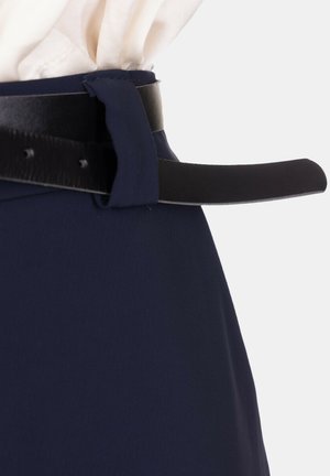 Primo piano di una gonna blu navy con una cintura in pelle nera infilata in un passante per cintura dello stesso tessuto, su uno sfondo chiaro.