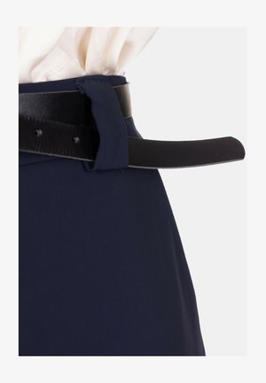 Primo piano di una gonna blu navy con una cintura in pelle nera infilata in un passante per cintura dello stesso tessuto, su uno sfondo chiaro.