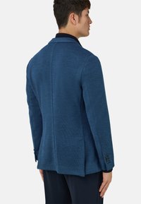 Niebieska marynarka z teksturowanego materiału, z ostrymi klapami i pojedynczym rozcięciem z tyłu. Charakteryzuje się guzikami na rękawach oraz dopasowanym krojem.