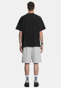 Czarny bawełniany t-shirt z krótkimi rękawami, połączony z szarymi szortami. Tył jest gładki, z okrągłym dekoltem i luźnym krojem.