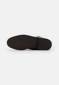 Suela de zapato de cuero marrón con un fondo de goma negra texturizada. Presenta texto grabado y un borde superior liso.