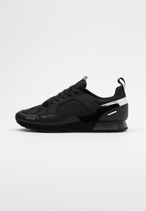 Baskets basses noires avec lacets, empiècements texturés, accent blanc au talon et marquage "Cruyff" sur le côté avant.