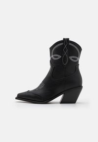 Black leather cowboy boot with pointed toe, stacked heel, white stitching accents, and decorative details on the upper part.