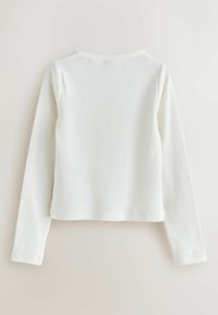 Langsleeve, aansluitend top van zacht wit ribmateriaal. Heeft een ronde halslijn en een cropped zoom, met subtiele stiksels.