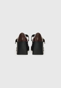 Chaussures à plateforme en cuir verni marron avec un talon texturé noir, dotées d'une bride de cheville et d'un design à bout arrondi.