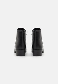 Pair of black leather ankle boots with stacked heels and back zippers, shown from the rear on a white background.