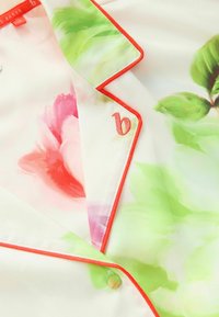 Floral zijden blouse met roze en groene aquarelpatronen, afgewerkt met een heldere rode rand en een klein geborduurd accent van de letter 'b'.