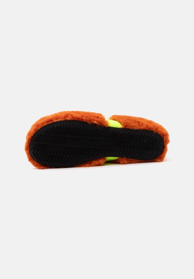 Vue de la semelle d’une pantoufle avec semelle en caoutchouc noir et dessus en tissu duveteux orange vif, révélant partiellement des détails intérieurs vert fluo.
