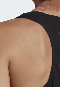 Svart linne med urringad rygg, tillverkat av mjukt bomullsmaterial. Tyget känns lent mot bar hud och framhäver axeln.