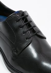 Scarpa da dress in pelle nera con texture liscia, chiusura con stringhe e dettagli di cucitura sottili. Presenta una punta arrotondata e un interno imbottito.