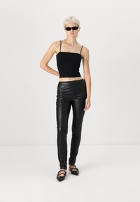 Zwarte aansluitende tanktop met dunne bandjes, gecombineerd met hooggetailleerde zwarte neplederen broek. Accessoires zijn onder andere kleine donkere zonnebrillen en platte schoenen.