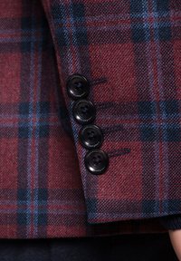 Mankiet marynarki w czerwoną i niebieską kratę z czterema czarnymi guzikami o teksturowanej powierzchni i detalami marki, podkreślający splot i wzór.