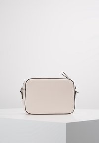 Prostokątna torebka w miękkim kremowym materiale, z czarnym obszyciem, zamknięciem na zamek błyskawiczny oraz wąskim paskiem z metalowymi akcentami.