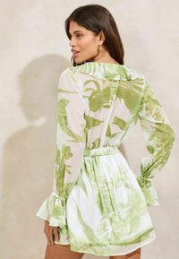 Viegls, caurspīdīgs kleitas modelis ar garām piedurknēm, ar zaļu ziedu rakstu uz balta fona, elastīgu jostasvietu un viļņainām aprocēm.