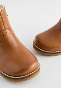 Bruine leren enkellaarsjes met een gladde afwerking, ronde neus en kleine perforaties. De zool is voorzien van een contrasterende gestikte detail.