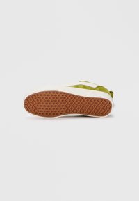 Sneaker verde in suede con dettagli bianchi e suola in gomma marrone texturizzata. Presenta un design a profilo basso e punta arrotondata.
