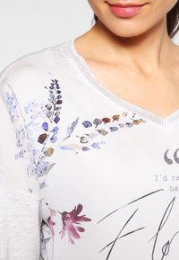 Top in leggero tessuto stampato floreale con scollatura a V e maniche corte. Il design presenta fiori multicolore in blu, viola e bordeaux.