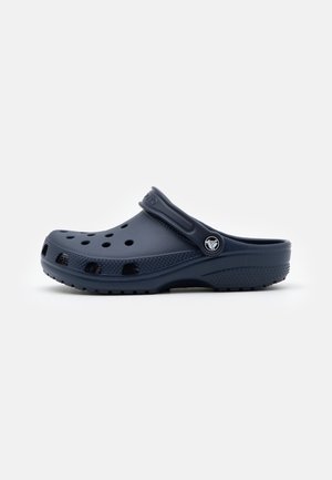 Mørkeblå slip-on træsko med ventilationshuller og en justerbar hælrem med en rund logo-knap på siden.