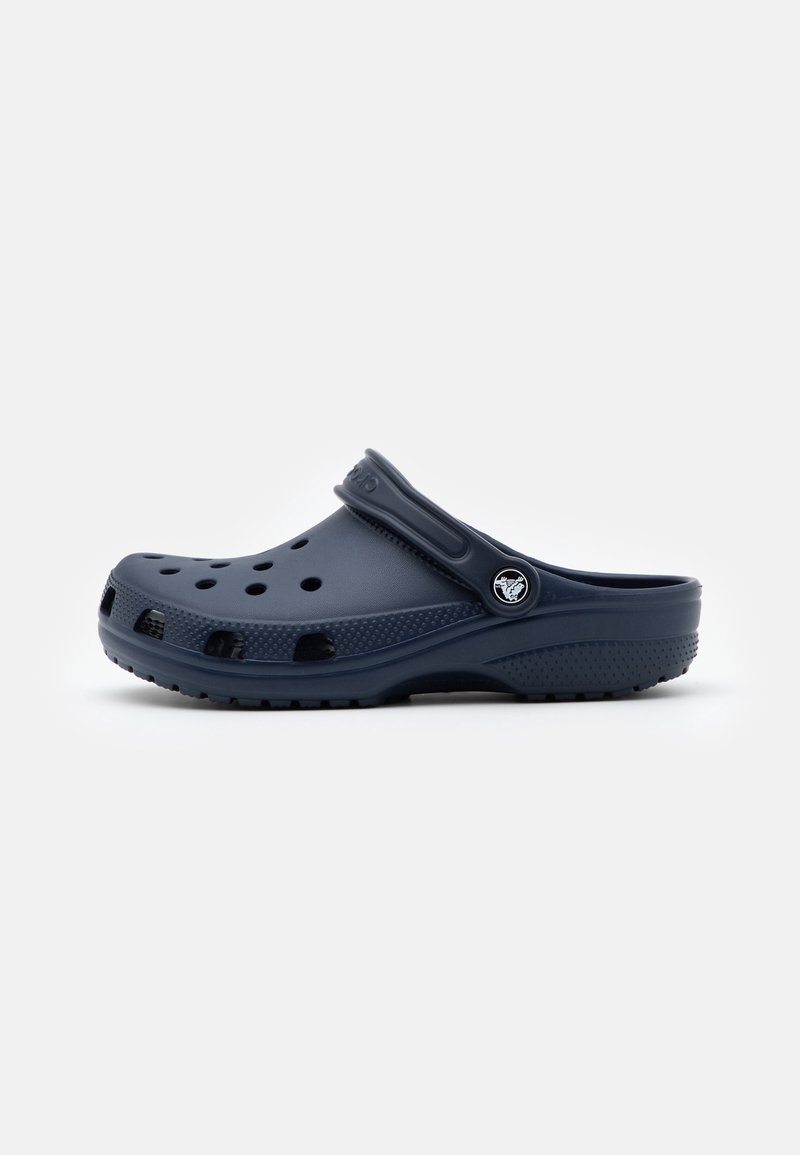 Sabot bleu foncé à enfiler avec des trous de ventilation et une bride de talon réglable avec un bouton logo rond sur le côté.
