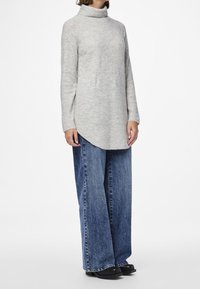 Szary sweter z wysokim kołnierzem, długimi rękawami i prostą sylwetką, zestawiony z szerokimi niebieskimi dżinsami i czarnym obuwiem.