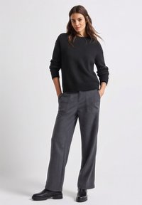 Zwarte gebreide trui met geribde zoom, gecombineerd met grijze wijd uitlopende broek met voorzakken. Model draagt zwarte enkellaarzen.