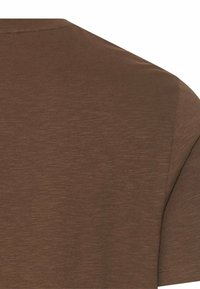 Nærbillede af en brun T-shirt med korte ærmer, der viser stoftekstur og sømme ved halsudskæringen på øvre ryg og skulderområde.