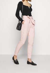 Svart randig långärmad bodysuit i kombination med högmidjade ljusrosa byxor med knytbälte och sidofickor. Svarta loafers och en liten väska.