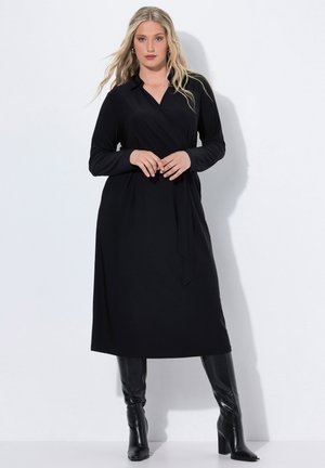 Schwarzes Wickelkleid mit langen Ärmeln und Kragen, aus einem glatten Stoff gefertigt. Hat einen Gürtel in der Taille und wird mit kniehohen schwarzen Stiefeln kombiniert.