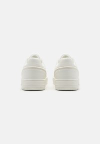 Para gładkich białych niskich sneakersów widocznych z tyłu na białym tle, podkreślających gładki skórzany materiał i gumowe podeszwy.