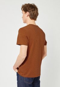 Bruine, korte mouwen t-shirt met een gestructureerde, melange stof. Klassieke ronde hals en een ontspannen pasvorm, gecombineerd met donkerblauwe jeans.