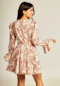 Vestido floral en rosa y beige con mangas abullonadas y puños acampanados. La tela texturizada presenta patrones florales y acentos de cuentas a lo largo del dobladillo.