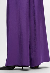 Paarse wijde broek van een gekreukt materiaal, met een gladde textuur en een hielaccent dat onderaan zichtbaar is.