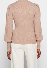 Jersey de canalé color beige rosa con mangas largas abullonadas y cintura ajustada, confeccionado con un tejido de punto suave y texturizado. Panel trasero liso.