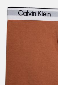 Brune bomullsblanding boxertruse med en hvit og grå elastisk midjebånd med "Calvin Klein"-logo i svart. Glatt tekstur, tettsittende design.