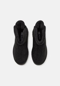 Botine negre la gleznă, cu căptușeală moale, asemănătoare cu blana, și partea superioară din material texturat. Au părți elastice pentru a fi ușor de purtat și o talpă robustă din cauciuc.