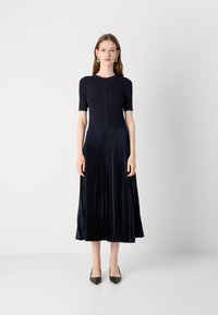 Navy blue pleated dress with short sleeves, ribbed bodice, and flowing skirt. Worn with black pointed-toe heels for a sleek look.